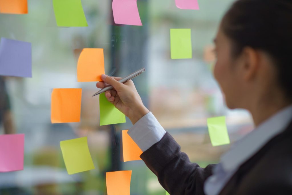 Person writing on colorful sticky notes attached to a glass wall.