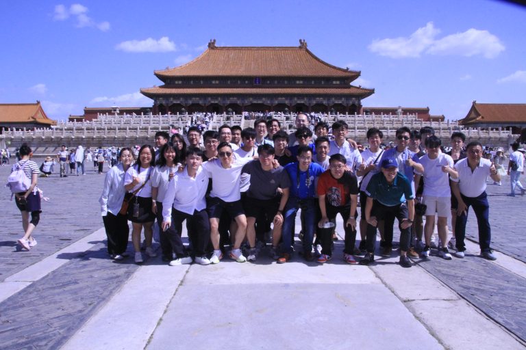 Group of people posing for photo in front of traditional Chinese palace under blue sky.