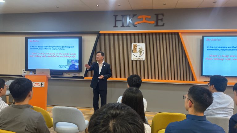 Speaker presenting at HK工E event, addressing audience with motivational quote on screens.