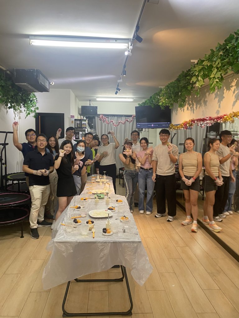 Group of people smiling and holding food at a decorated indoor event.