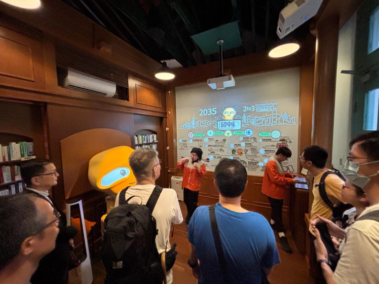 Group viewing interactive carbon neutrality exhibit with presenter and large projection screen.