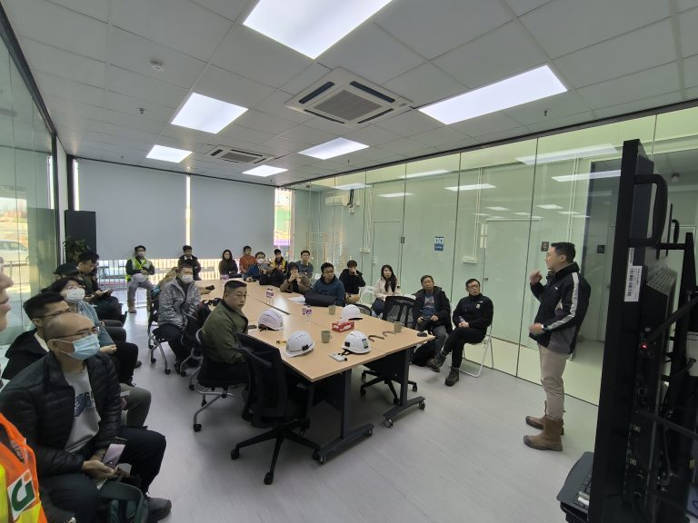 Group meeting in conference room with presenter and attendees wearing safety gear.