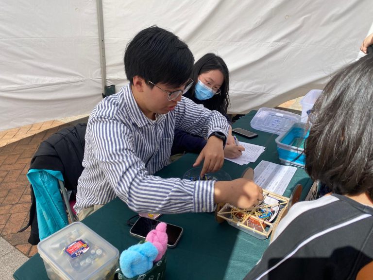 People collaborating on a hands-on activity at an outdoor event under a tent.
