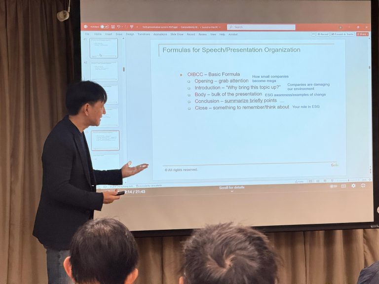 Speaker presenting slide on speech organization formulas to audience in conference room.