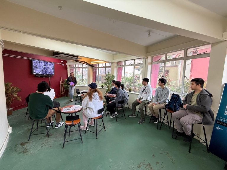 Group of people seated in a room listening to a presenter near a screen.