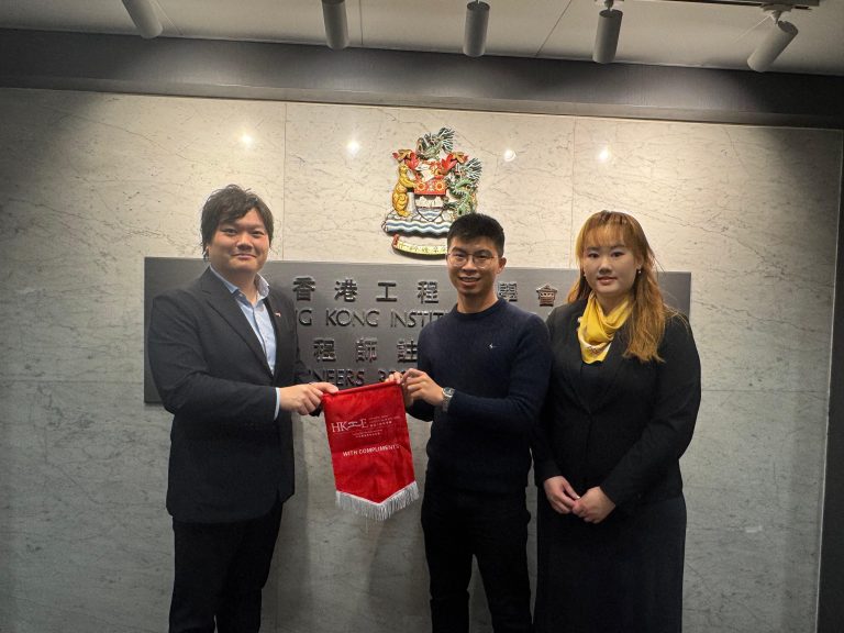 Three people posing in front of Hong Kong Institution of Engineers plaque, exchanging a red commemorative flag.
