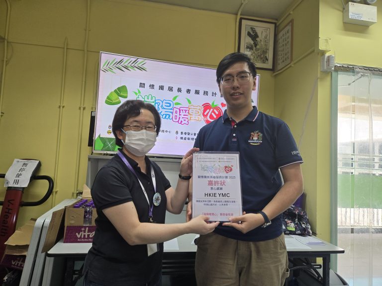 Two people holding a certificate for HKIE YMC at a community service event.