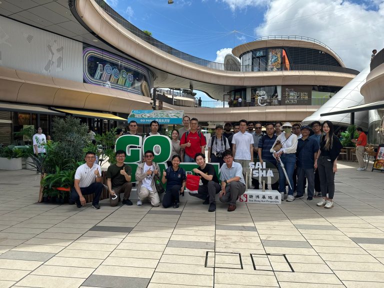 "Group of people posing for photo in modern outdoor shopping complex with large ""GO"" sign."